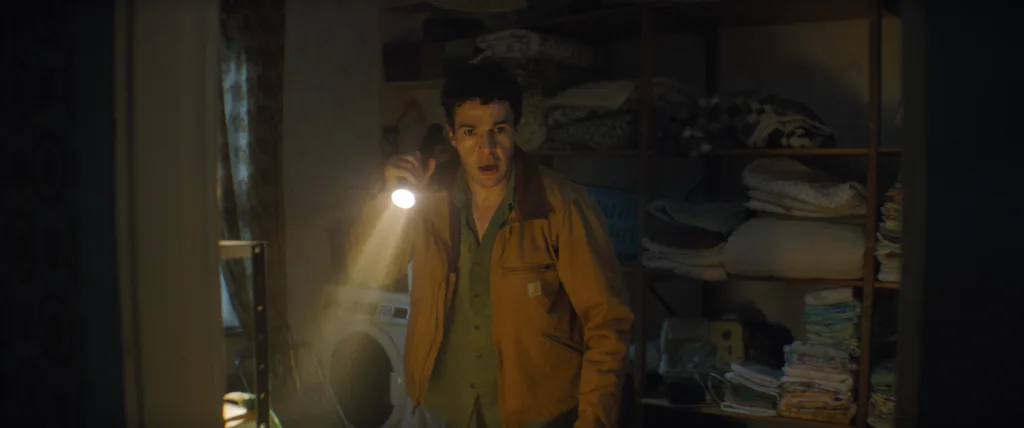 Wolf Man Ο Christopher Abbott σε σκηνή από το Wolf Man, κρατώντας φακό σε ένα σκοτεινό δωμάτιο
