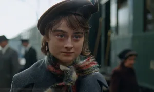 Raffey Cassidy in The Brutalist (2024) - A close-up portrait showing the actress in period winter attire with a brown beret and colorful knit scarf