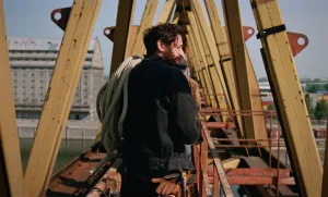 Adrien Brody in The Brutalist (2024) carrying construction rope, photographed from behind against industrial scaffolding and architectural framework